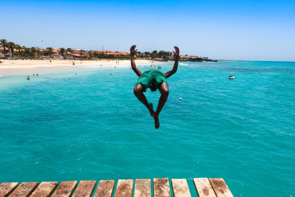 Teenage Cape verdean boy jumping on the turquoise  water of Santa Maria beach in Sal Cape Verde - Cabo Verde